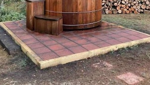 A wood-burning stove with a chimney, surrounded by a brick platform, set in a forested area. - LINVILLE Nostalgic Mountain Farm Glamping Camper on Wedding Venue, 10 acre farm  (Linville)