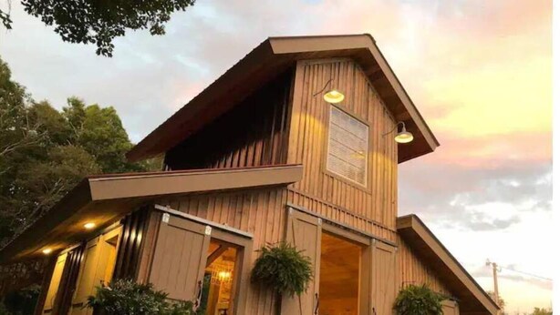 A two-story wooden house with a sloped roof, large windows, and a well-lit entrance. - LINVILLE Nostalgic Mountain Farm Glamping Camper on Wedding Venue, 10 acre farm  (Linville)