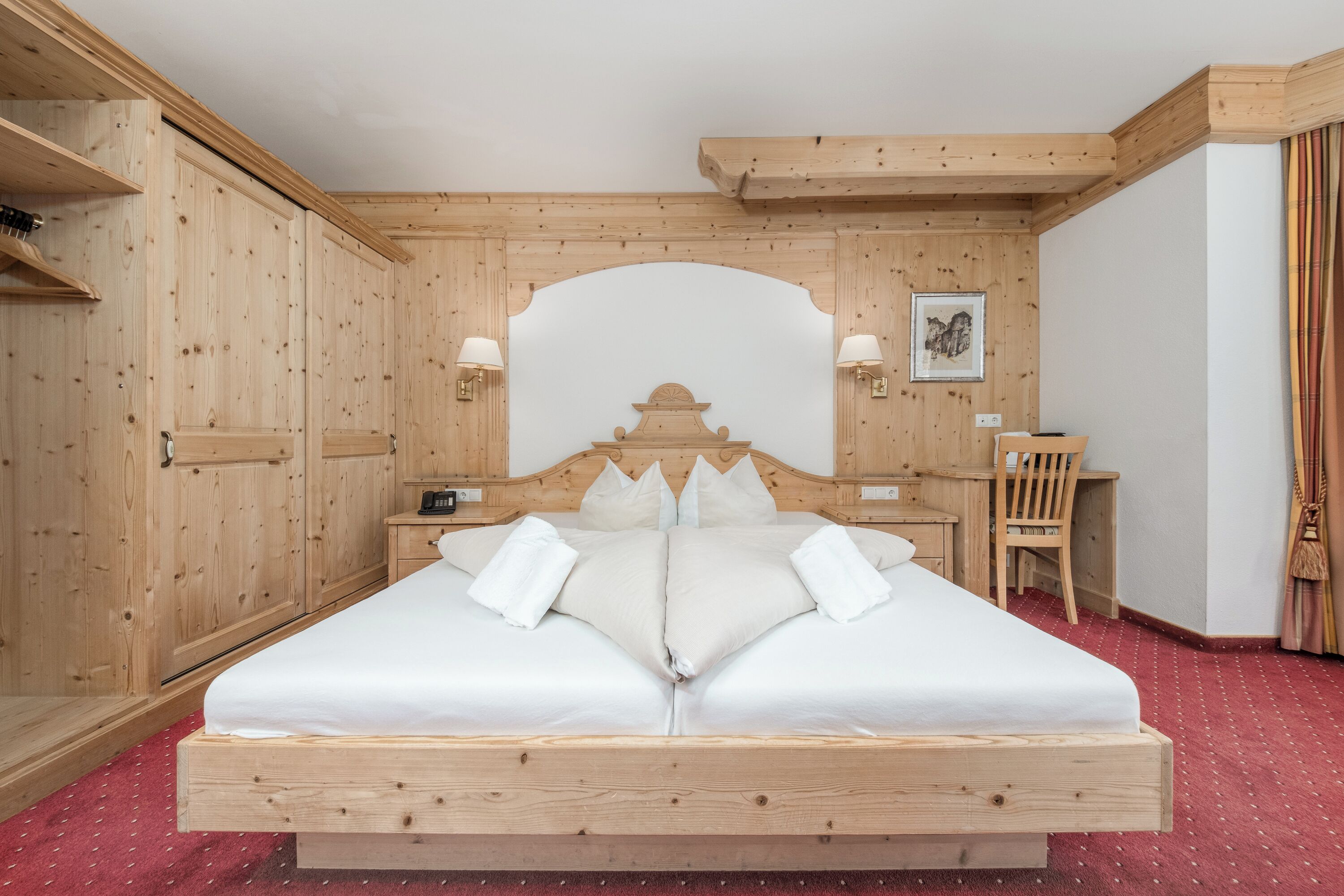 A wooden bedroom with a bed, bedside tables, a desk, and a chair.