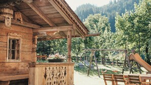 A rustic wooden cabin with a porch, a wooden table, and a swing set in a forested area. - Alpenhotel Tirolerhof (Gerlos)