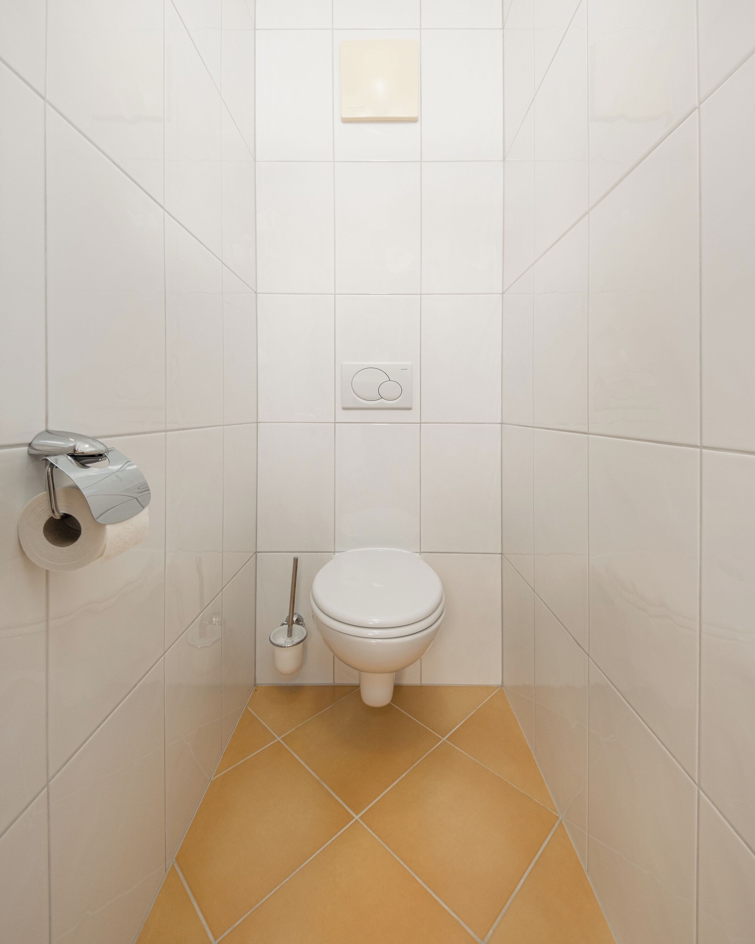 Un bagno piccolo e pulito rivestito di piastrelle bianche, con il water, un porta carta igienica e un bidet.