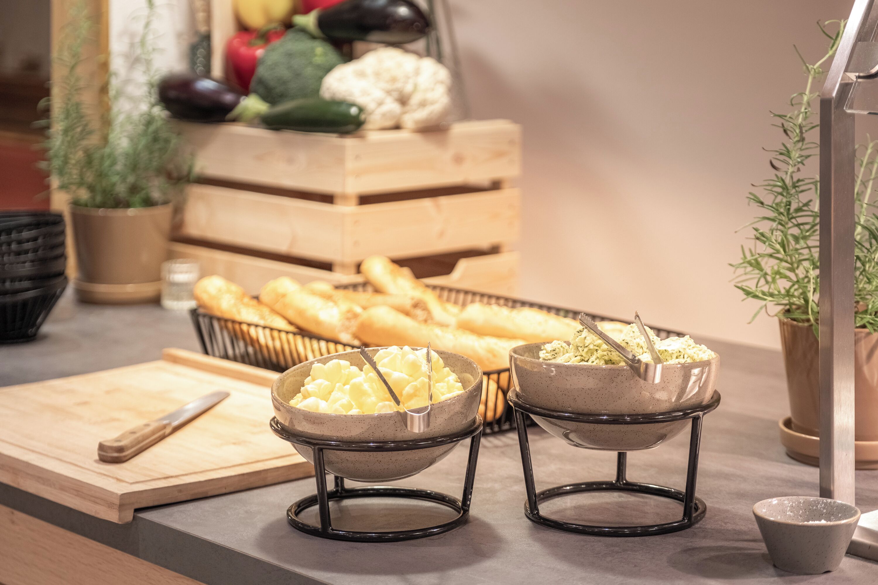 Un buffet composé de deux plats de nourriture, d’une planche à découper et d’un panier de pain.