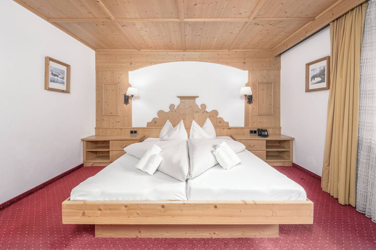 A wooden-framed bed with white linens, a wooden headboard, bedside tables with lamps, and a red carpeted floor.