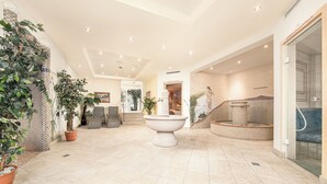 A spacious lobby with a central fountain, seating area, and a sauna entrance. - Alpenhotel Tirolerhof (Gerlos)