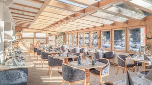 A restaurant with wooden beams and large windows, offering views of a snowy landscape. - Alpenhotel Tirolerhof (Gerlos)