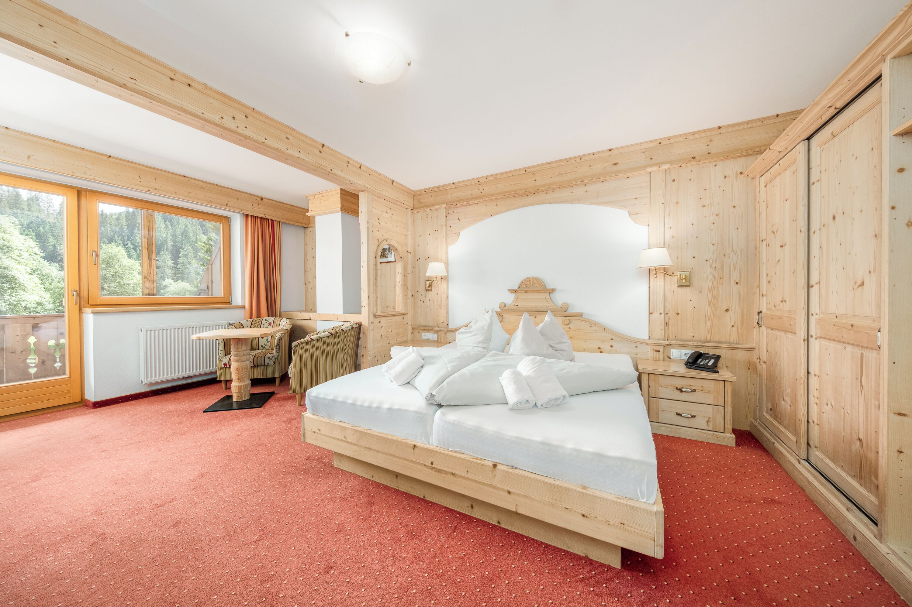 A wooden-paneled bedroom with a large bed, a desk, and a window with curtains.