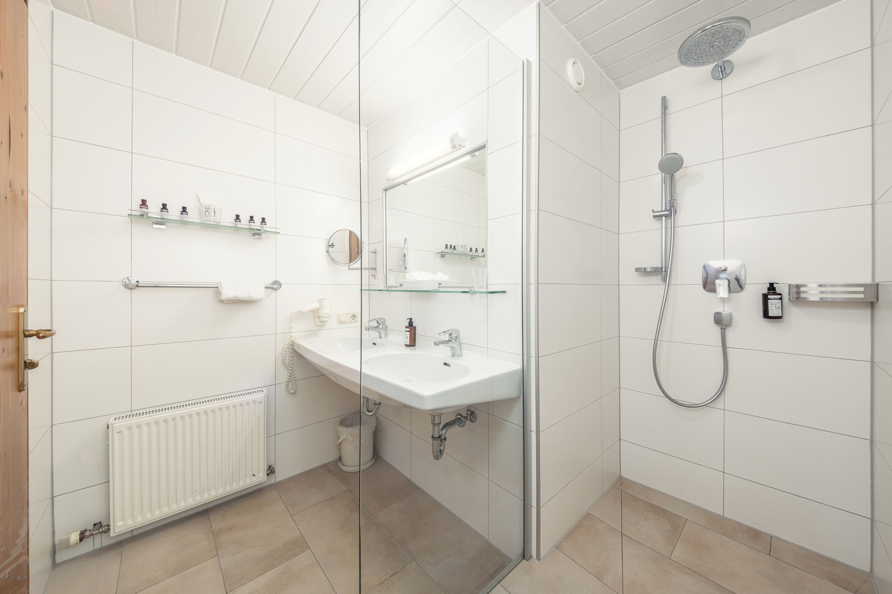 Un baño moderno con cabina de ducha de vidrio, un lavamanos blanco con espejo y un perchero para toallas.