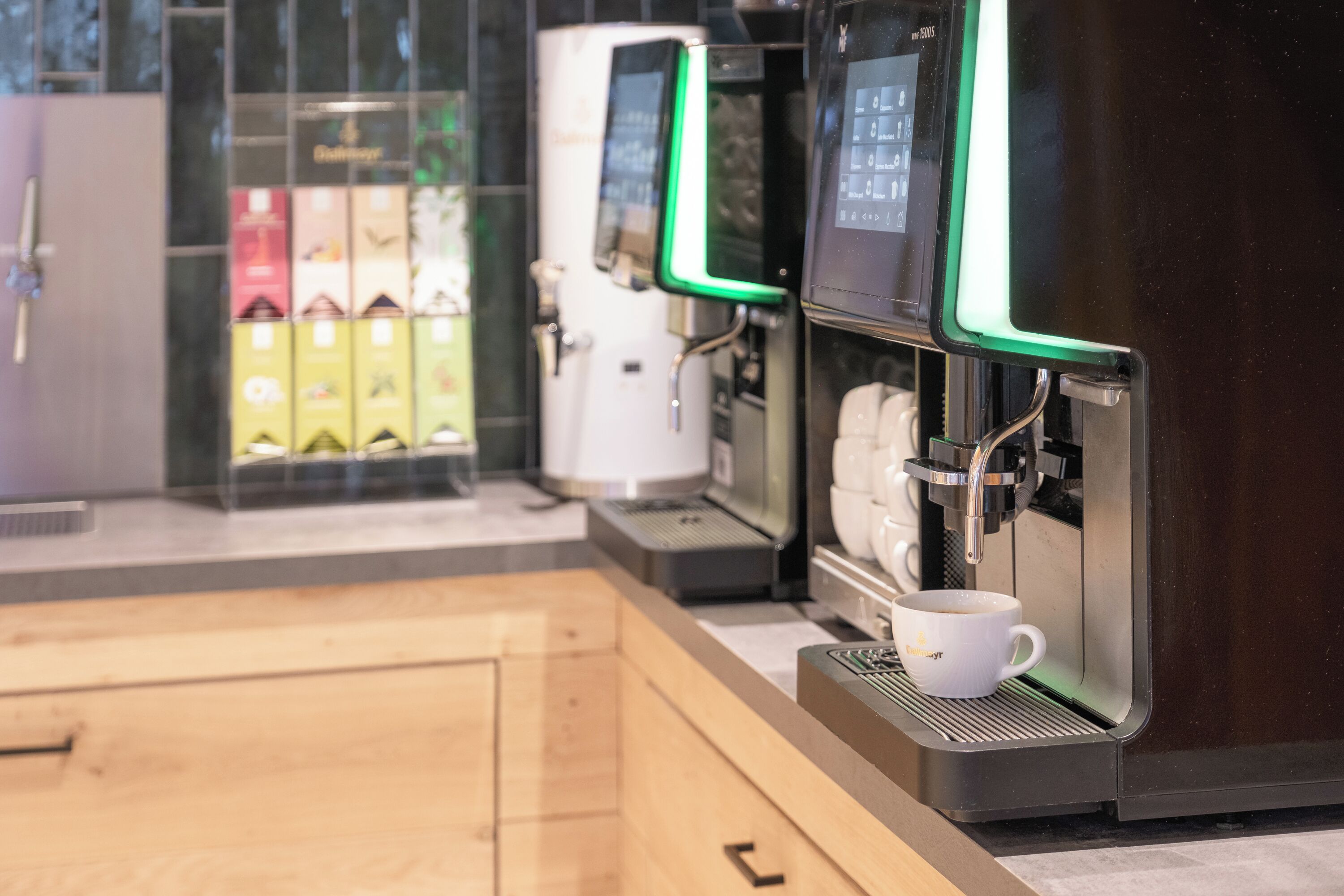 Une machine à café dotée d’un écran numérique, une tasse de café et un distributeur automatique proposant diverses boissons.