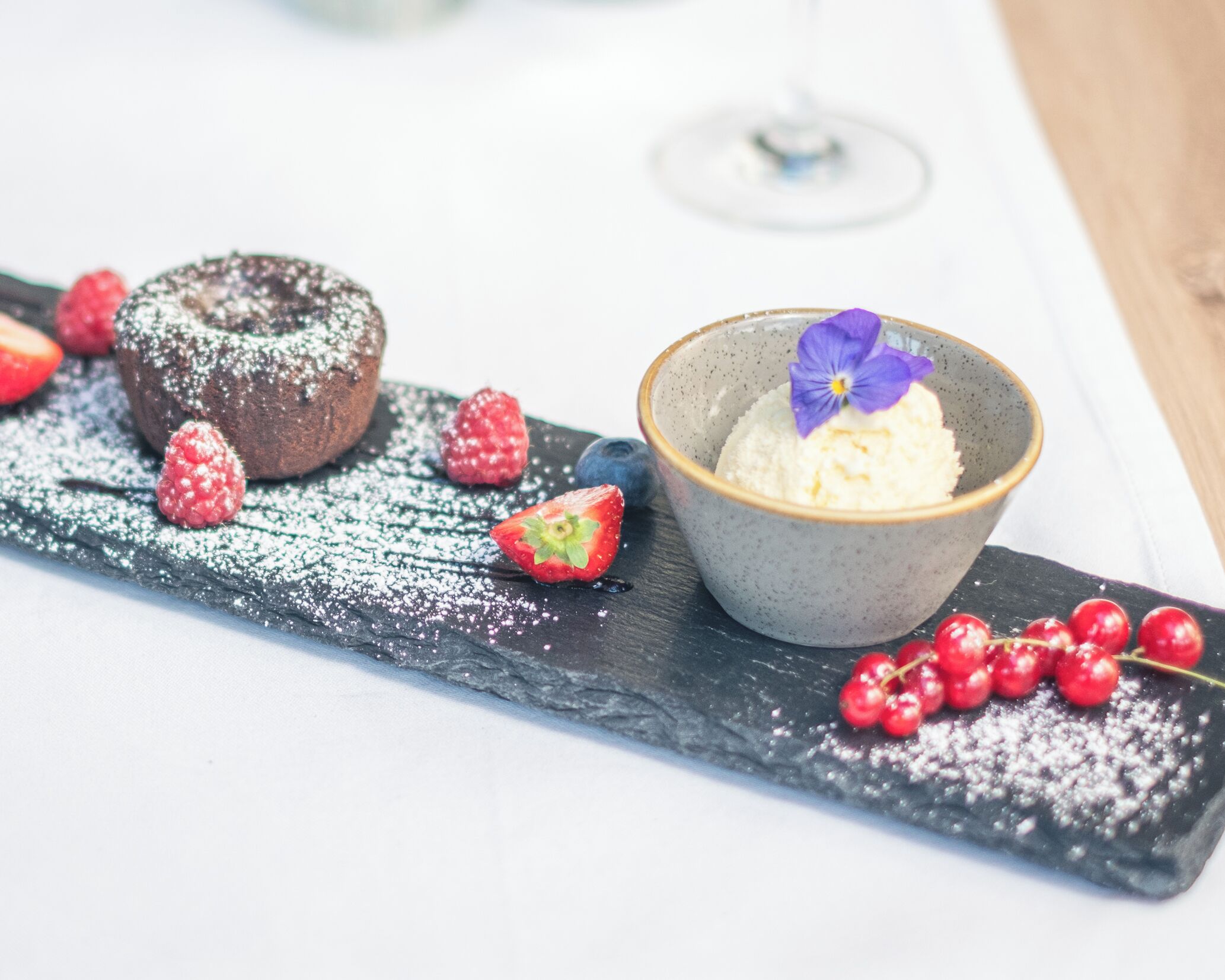 A dessert plate with a chocolate cake, strawberries, blueberries, and a bowl of ice cream with a flower on top.