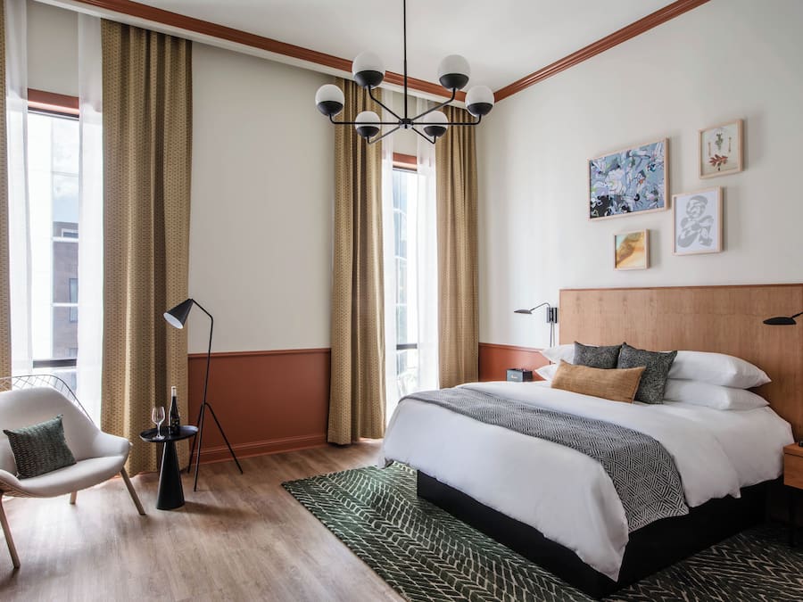 A hotel room with a large bed, a chair, a desk, and a window with curtains.