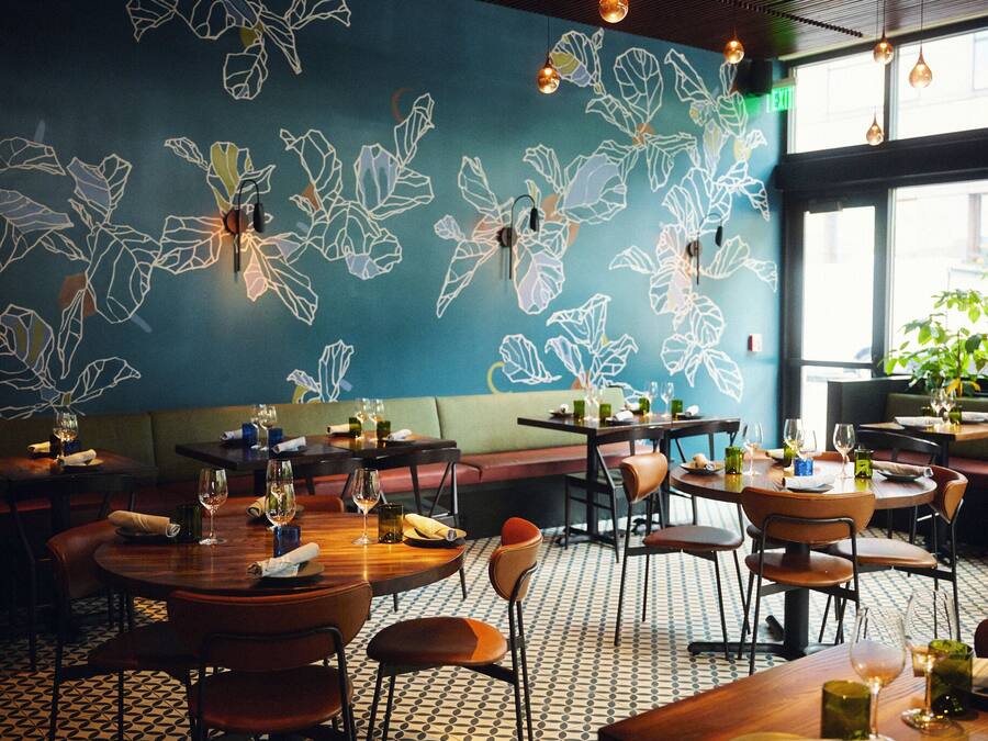 L’intérieur d’un restaurant, avec des tables et des chaises, un sol à motifs et un mur orné de motifs végétaux.