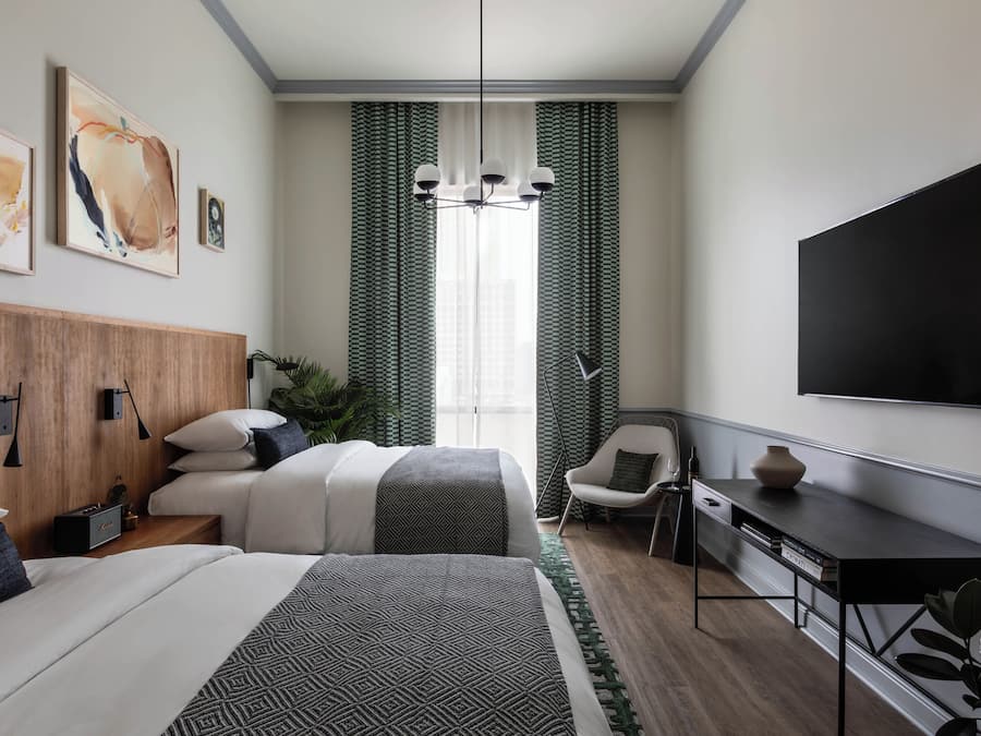 A modern hotel room with two beds, a desk, a TV, and artwork on the walls.