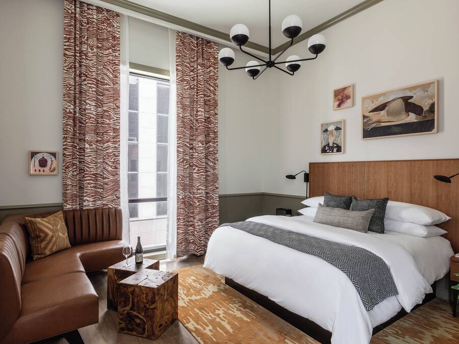 A modern bedroom with a large bed, a sofa, a wooden coffee table, and a chandelier.