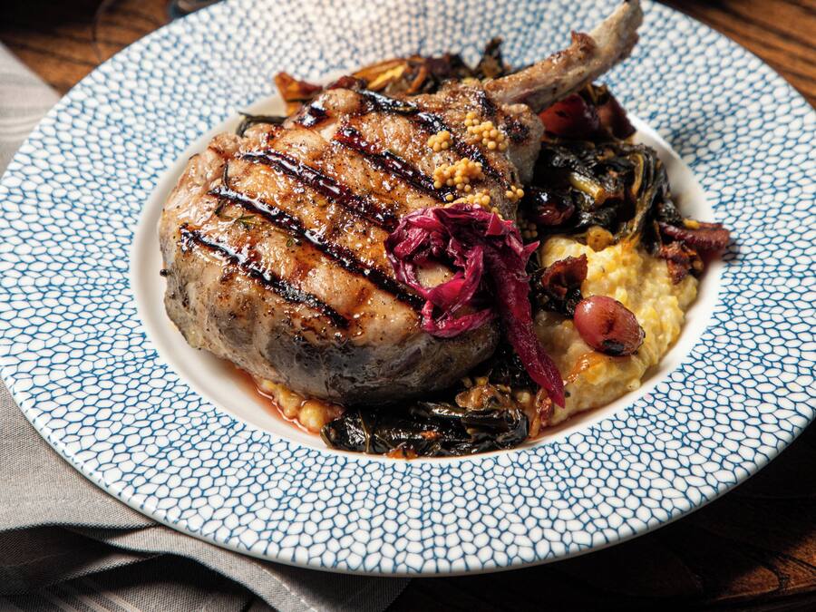 A plate of food with a lamb chop, vegetables, and a glass of wine.