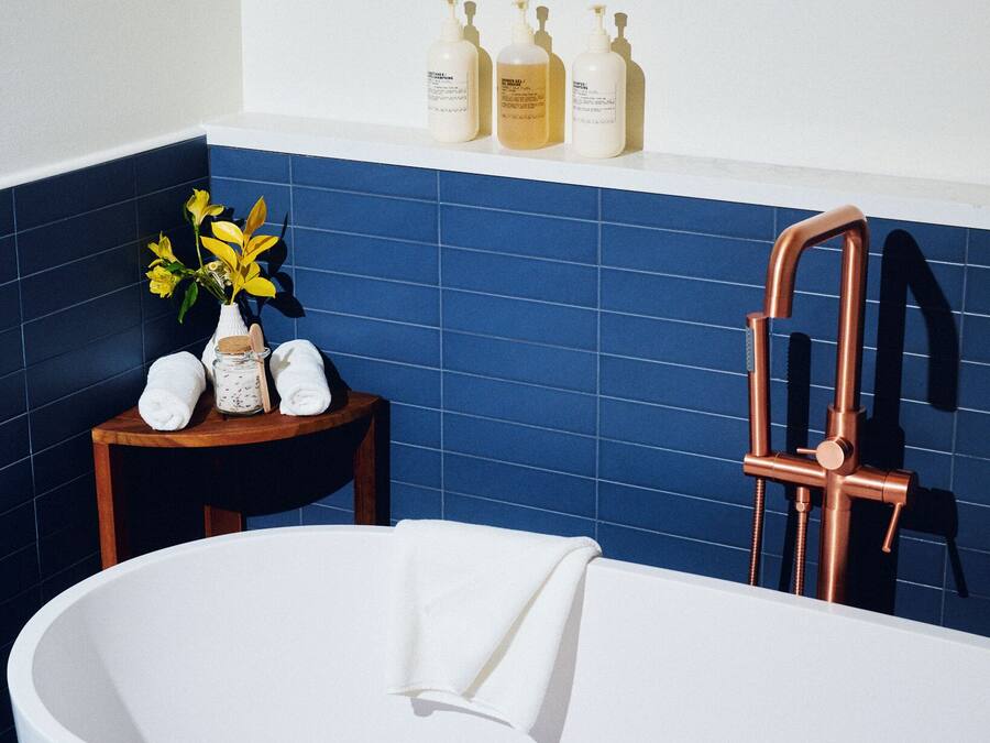A bathroom with a freestanding bathtub, a wooden stool, a vase with flowers, and toiletries on a shelf.