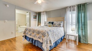 A bedroom with a bed, a ceiling fan, a bedside table, and a bathroom visible through an open door. - Pensacola Home w/ Private Dock - 7 Mi to Beaches (Pensacola)