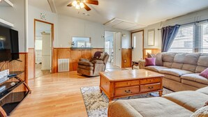 A spacious living room with a wooden floor, a ceiling fan, a television, a sofa, a coffee table, and a fireplace. - Pensacola Home w/ Private Dock - 7 Mi to Beaches (Pensacola)