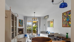 Una habitación con una mesa de madera, una cesta tejida, un sofá y un cuadro colorido en la pared.