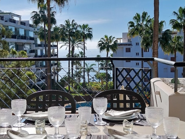 Enjoy a meal with a view of the sea from this outdoor dining area, featuring a table set with glassware and plates, and two comfortable chairs.