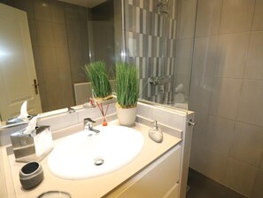 A modern bathroom with a white sink, two potted plants, a mirror, and a shower area.