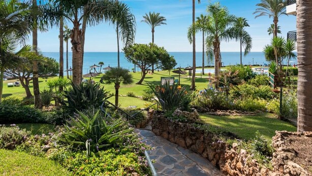 A tropical resort with palm trees, a stone pathway, and a view of the ocean. - 1370 Mi Capricho Calahonda Holiday Rental (Mijas)