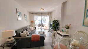 A modern living room with a sofa, a dining table, and chairs. There is a plant and a lamp on the table. - 1370 Mi Capricho Calahonda Holiday Rental (Mijas)