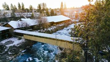A wooden bridge over a river with snow-covered buildings and trees in the background.