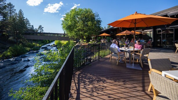 An outdoor dining area with tables and chairs, overlooking a river and surrounded by greenery. - Connect with Nature | 1 King + ADA rated (Bend)