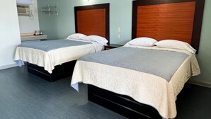 Ein Hotelzimmer mit zwei Betten, jeweils mit einem Holz-Kopfteil, einem grauen Teppich und einer hellblauen Wand.