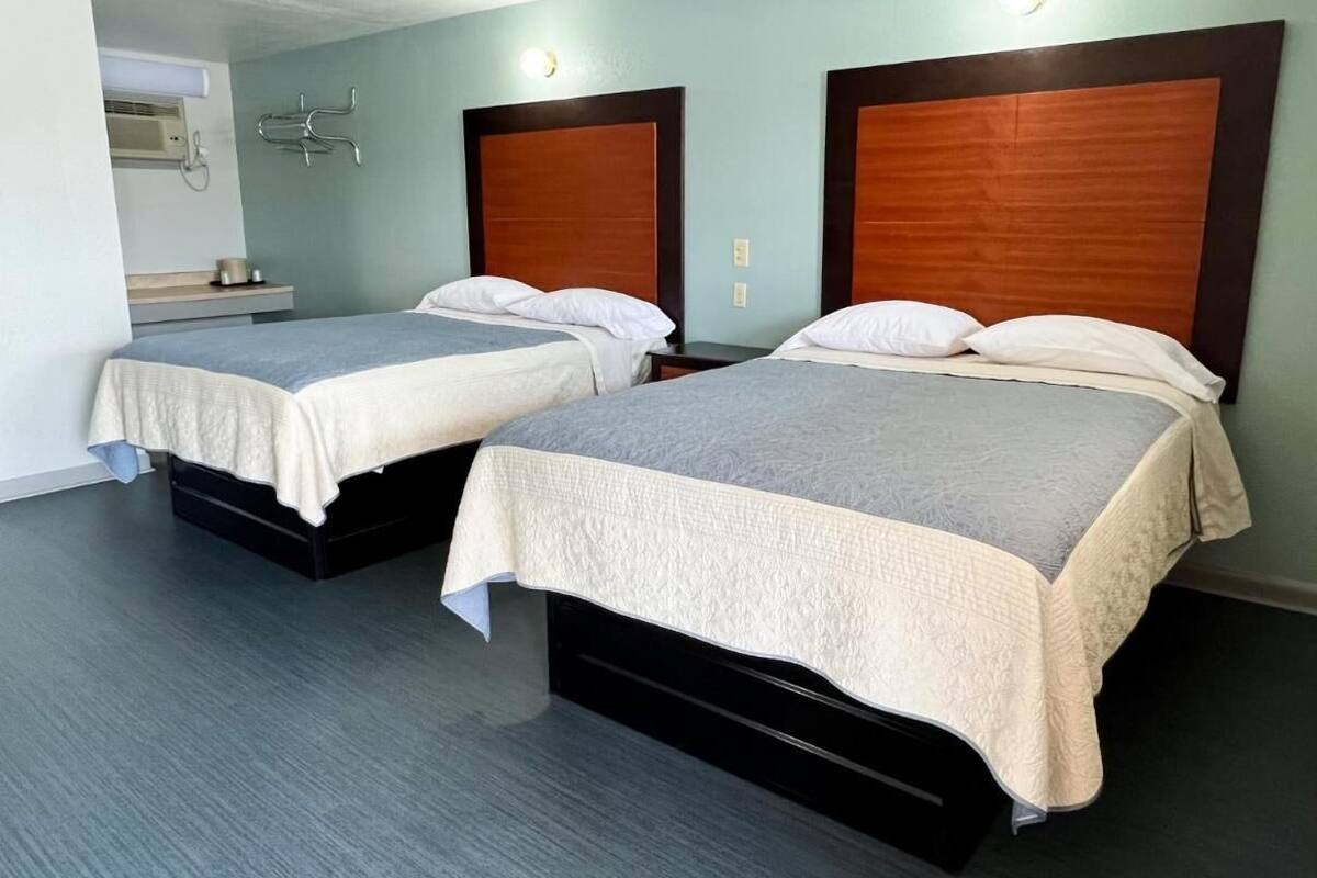 A hotel room with two beds, each with a wooden headboard, a grey carpet, and a light blue wall.