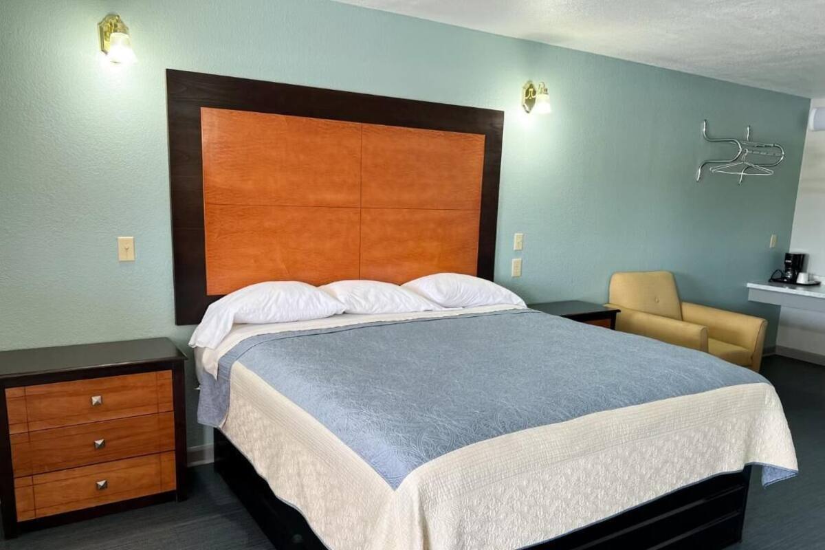 A bedroom with a large bed, a nightstand, a chair, and a desk with a lamp.