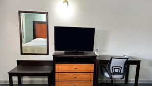 Ein Hotelzimmer mit dunklem Holztisch, Fernseher, Stuhl und Spiegel an der Wand.