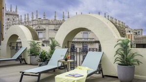 A rooftop terrace with lounge chairs, potted plants, and a decorative archway.