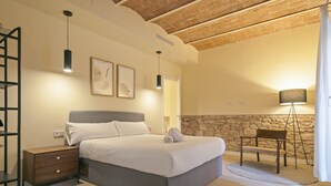 A bedroom with a bed, bedside table, lamp, and a stone wall.