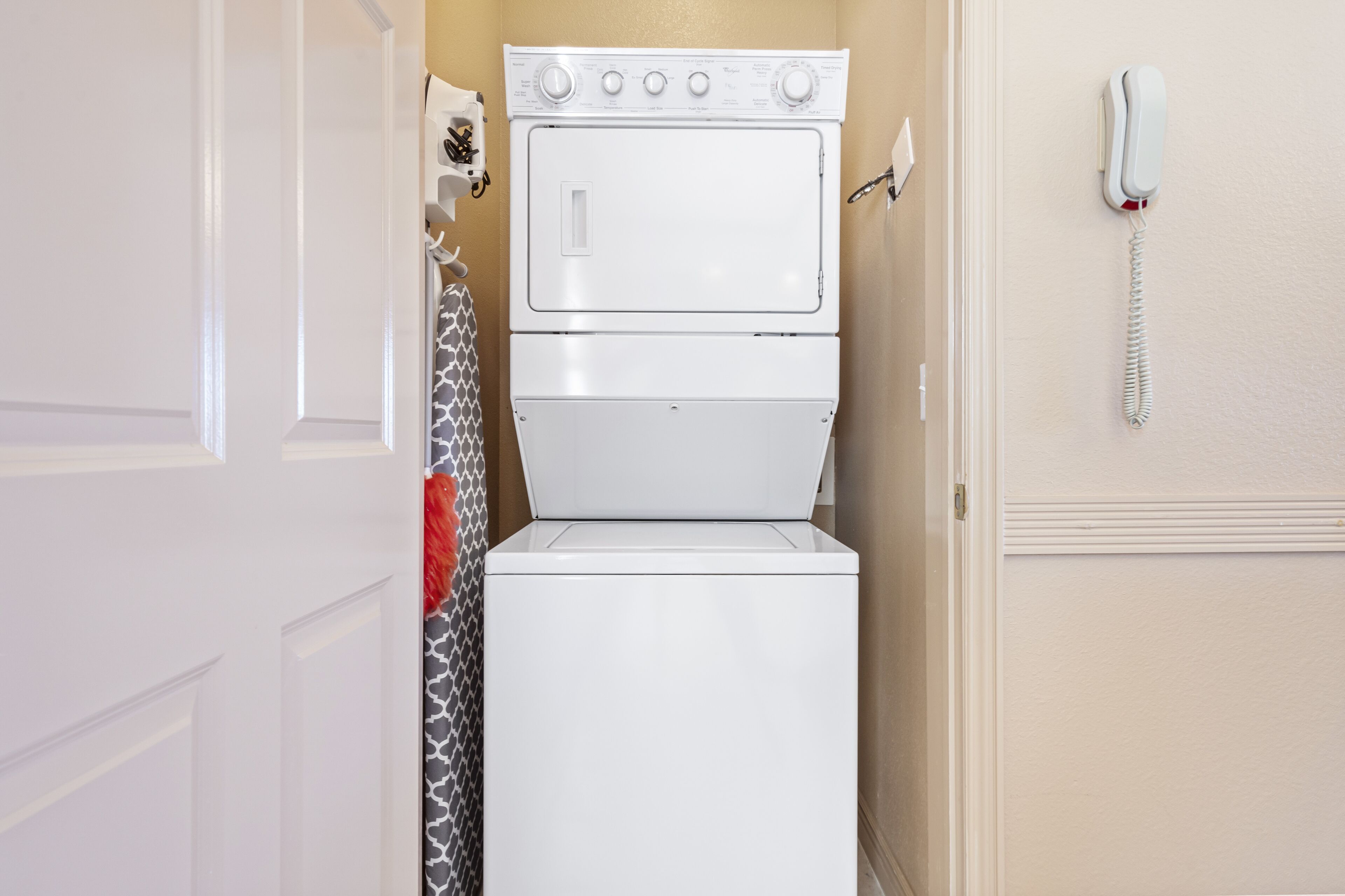 A compact washer and dryer unit in a small laundry room with a telephone mounted on the wall.