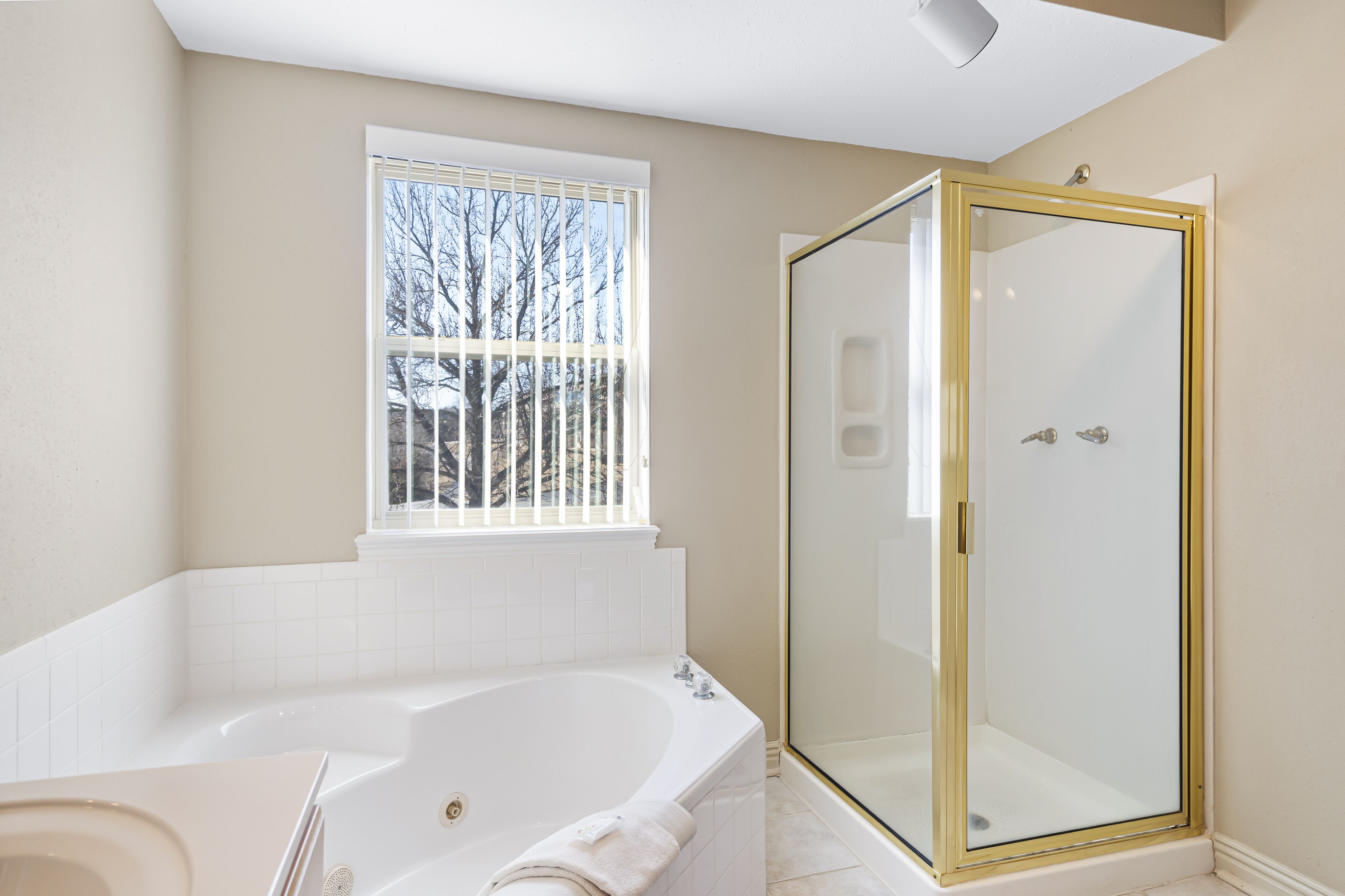 A bathroom with a large bathtub, a glass-enclosed shower, and a window with a view of trees.