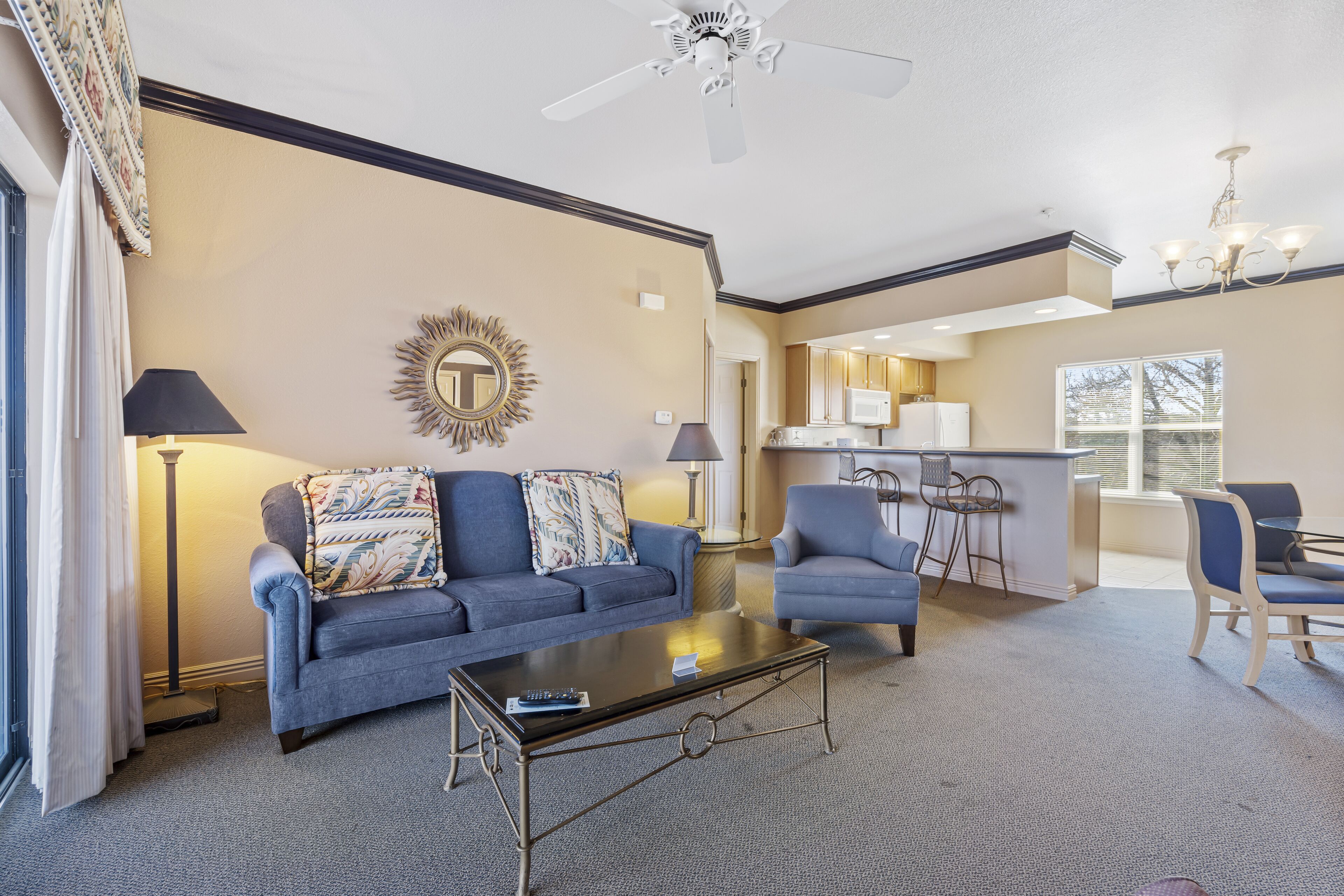 A living room with a sofa, armchair, coffee table, and a kitchenette in the background.