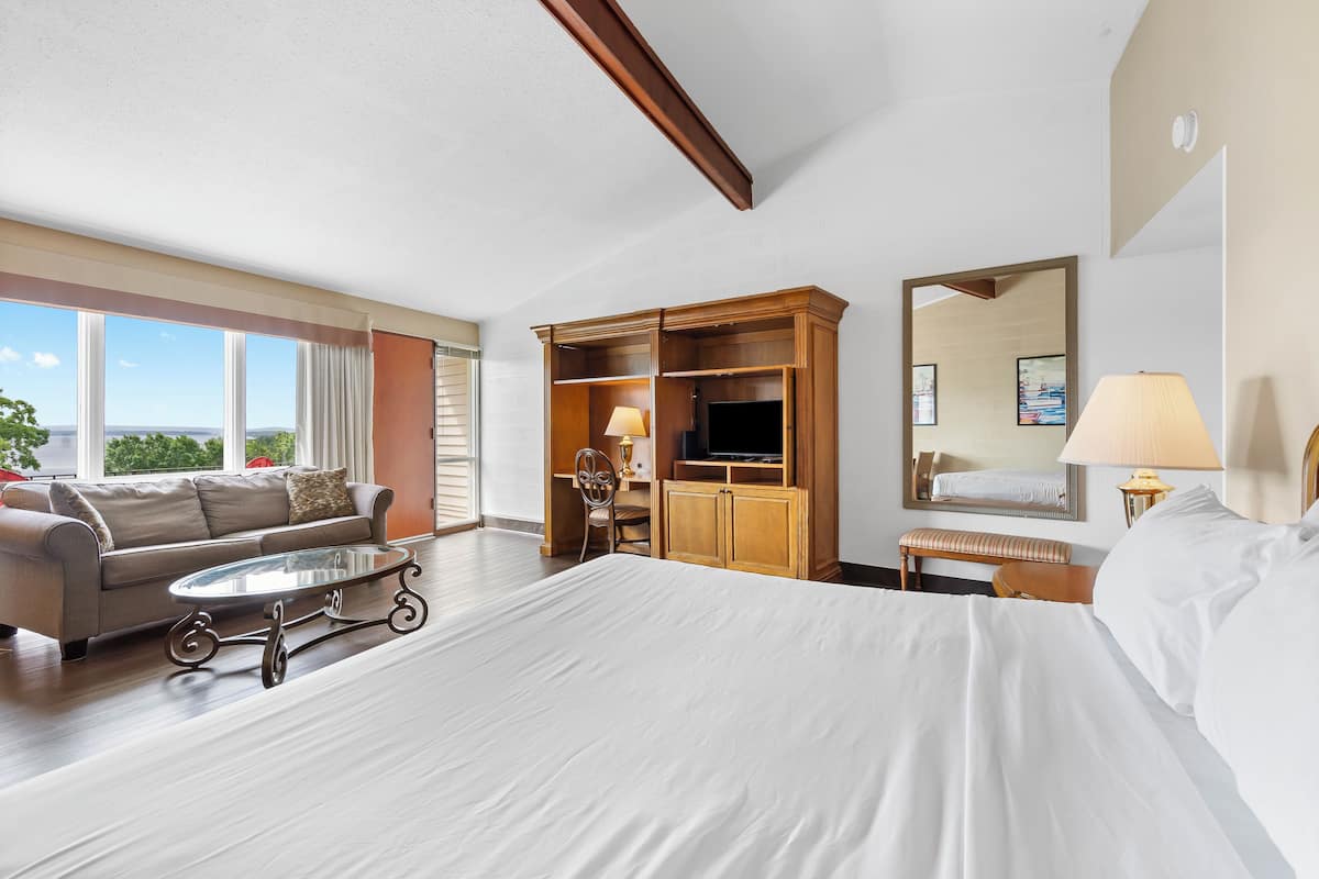 Une chambre d’hôtel avec un grand lit, un canapé, une télévision, un bureau et une fenêtre donnant sur un beau paysage.