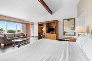 Quarto de hotel com uma cama grande, sofá, televisão, escrivaninha e janela com vista.