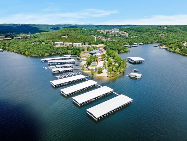 Vista aérea de um resort à beira do lago, com várias embarcações atracadas, uma ilha central com edifícios e vegetação ao redor.