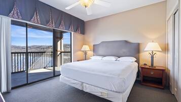 A hotel room with a large bed, two bedside lamps, a ceiling fan, and a view of a mountainous landscape through a sliding glass door.