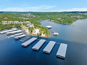 An aerial view of a lakeside hotel with multiple docked boats, a marina, and surrounding greenery.