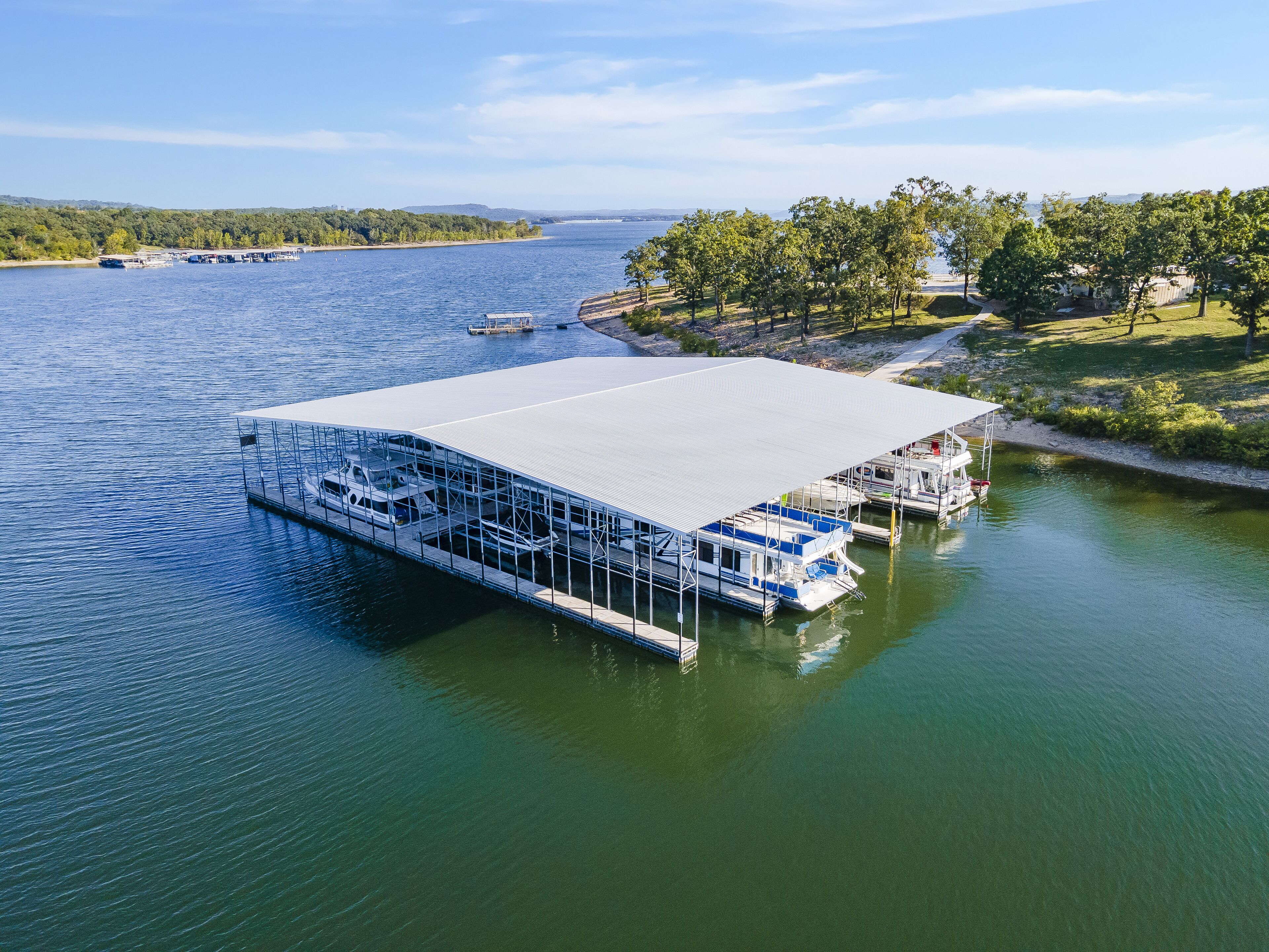 A floating structure with a covered deck and multiple levels, docked in a body of water with boats nearby.