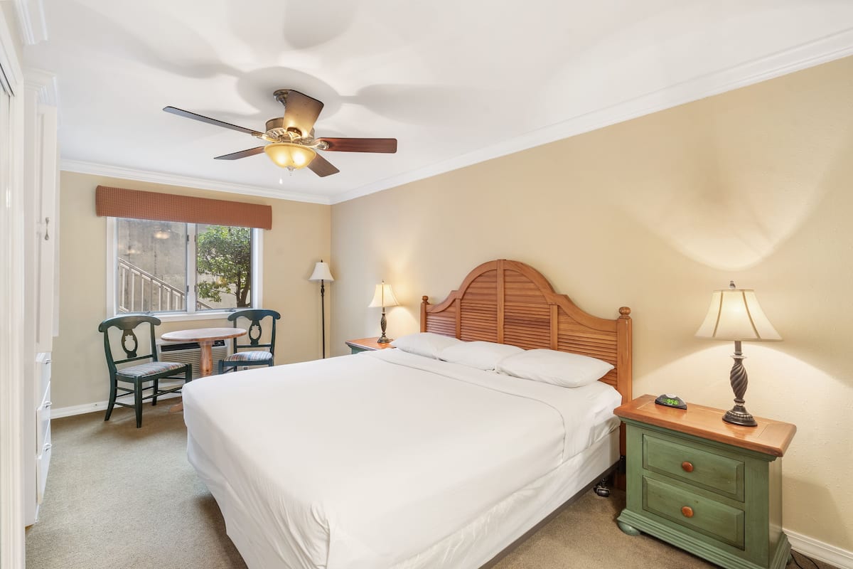 Une chambre bien rangée, avec un lit, une table de chevet, une lampe, une chaise et un ventilateur de plafond.
