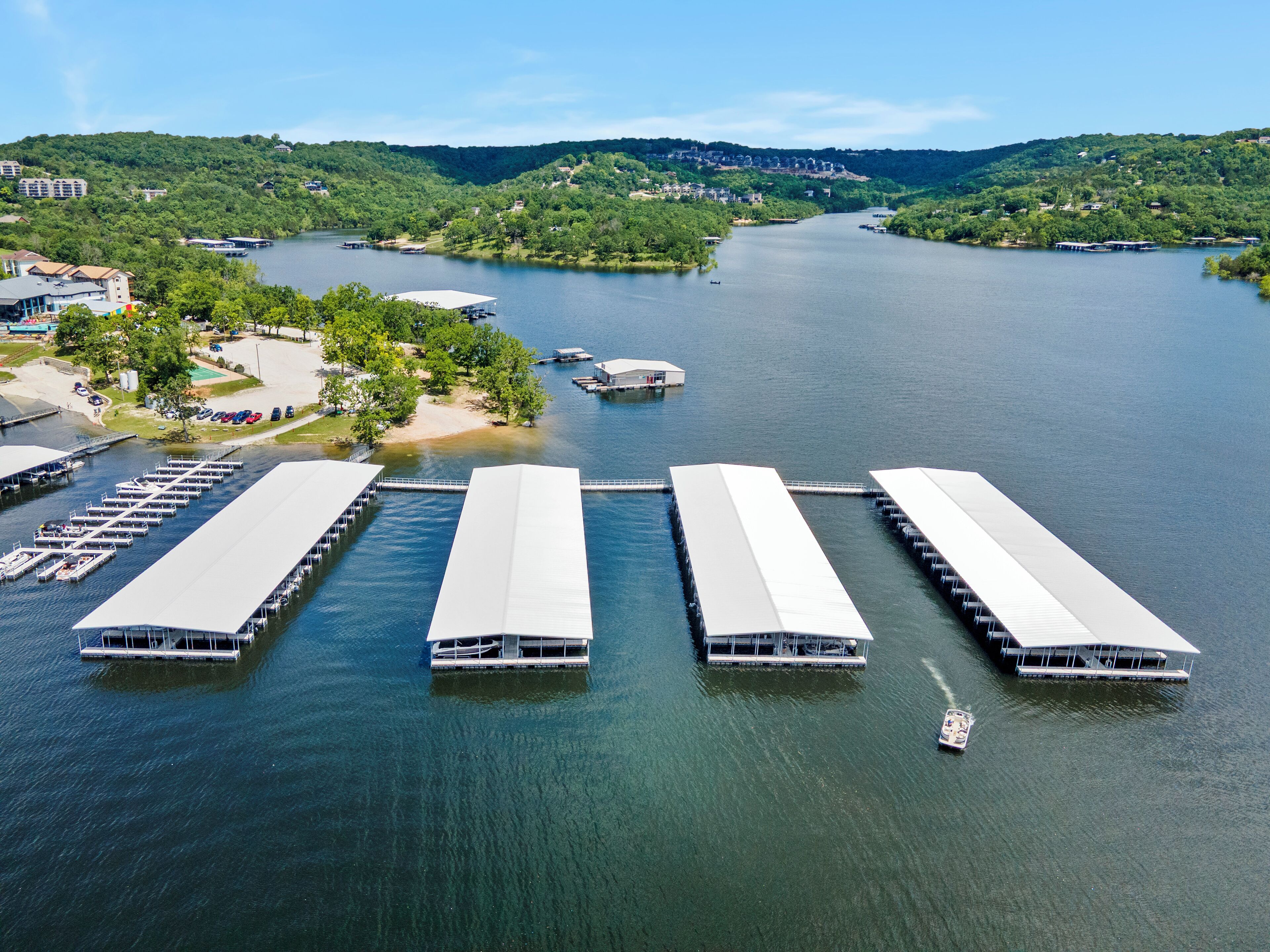 An aerial view of a marina with multiple docked boats, surrounded by lush greenery and hills in the background.