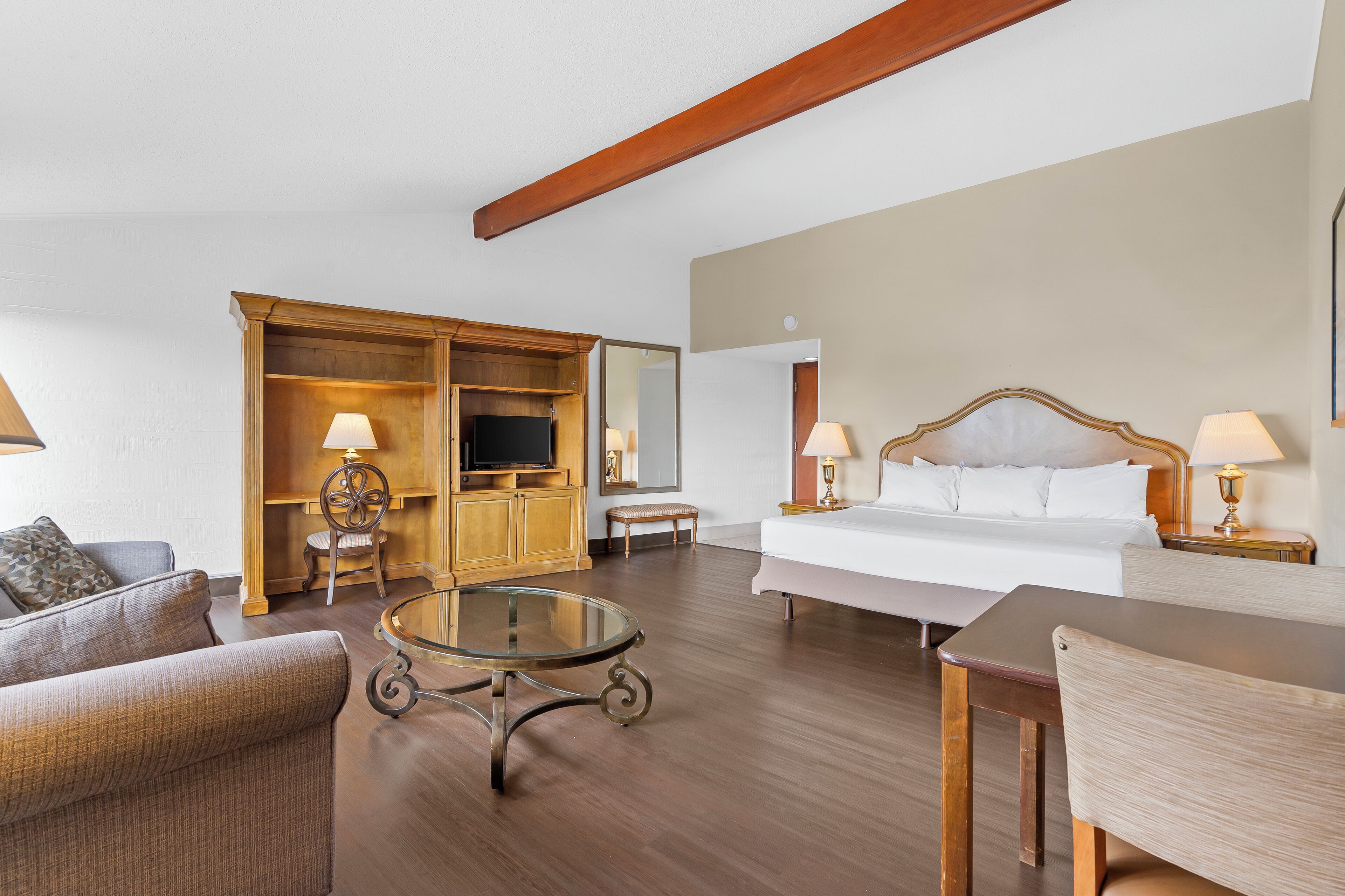 A hotel room with a bed, a sofa, a glass coffee table, a wooden cabinet, and a television.