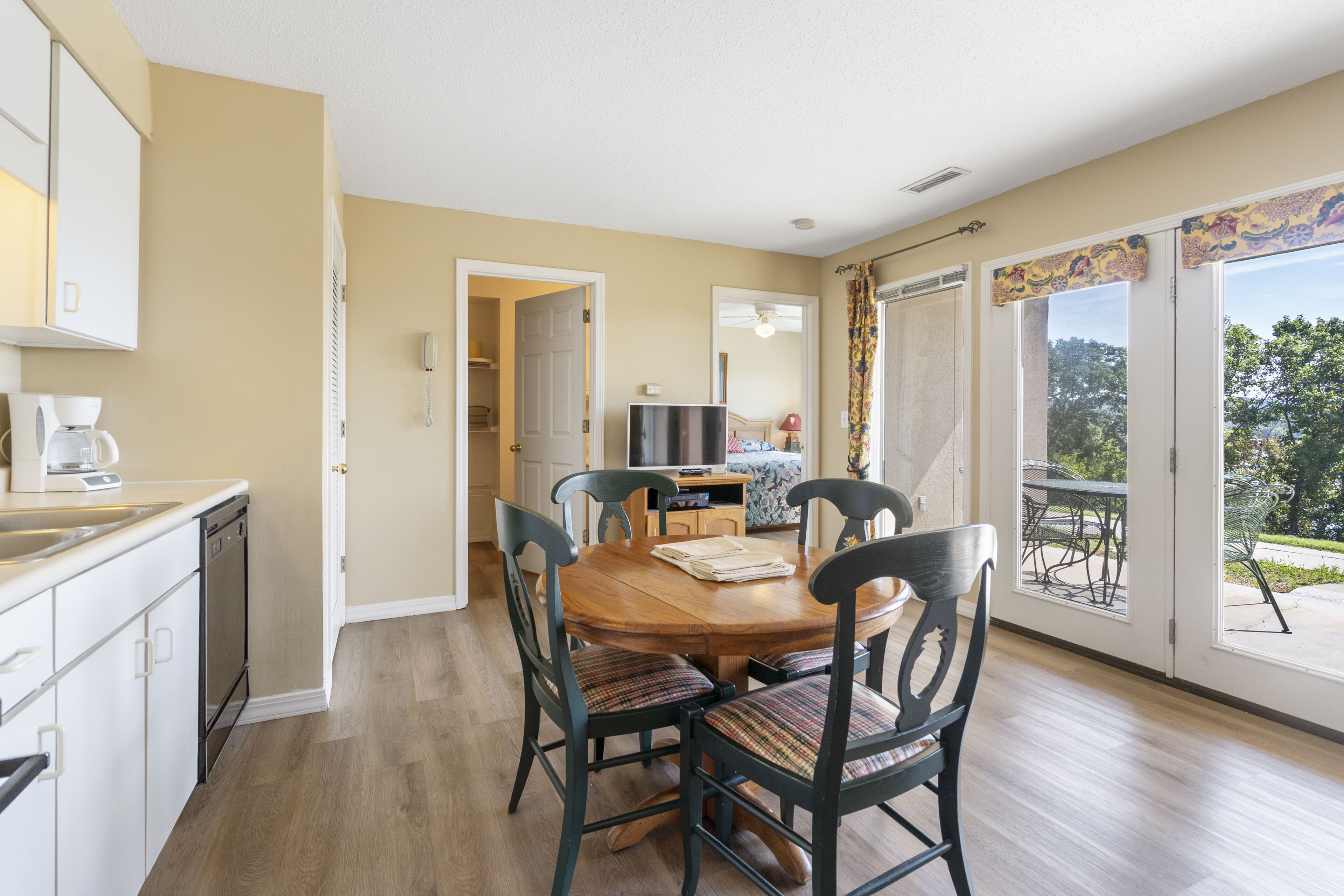 A dining area with a wooden table and chairs, a kitchen with a dishwasher, and a large sliding glass door leading to an outdoor patio.