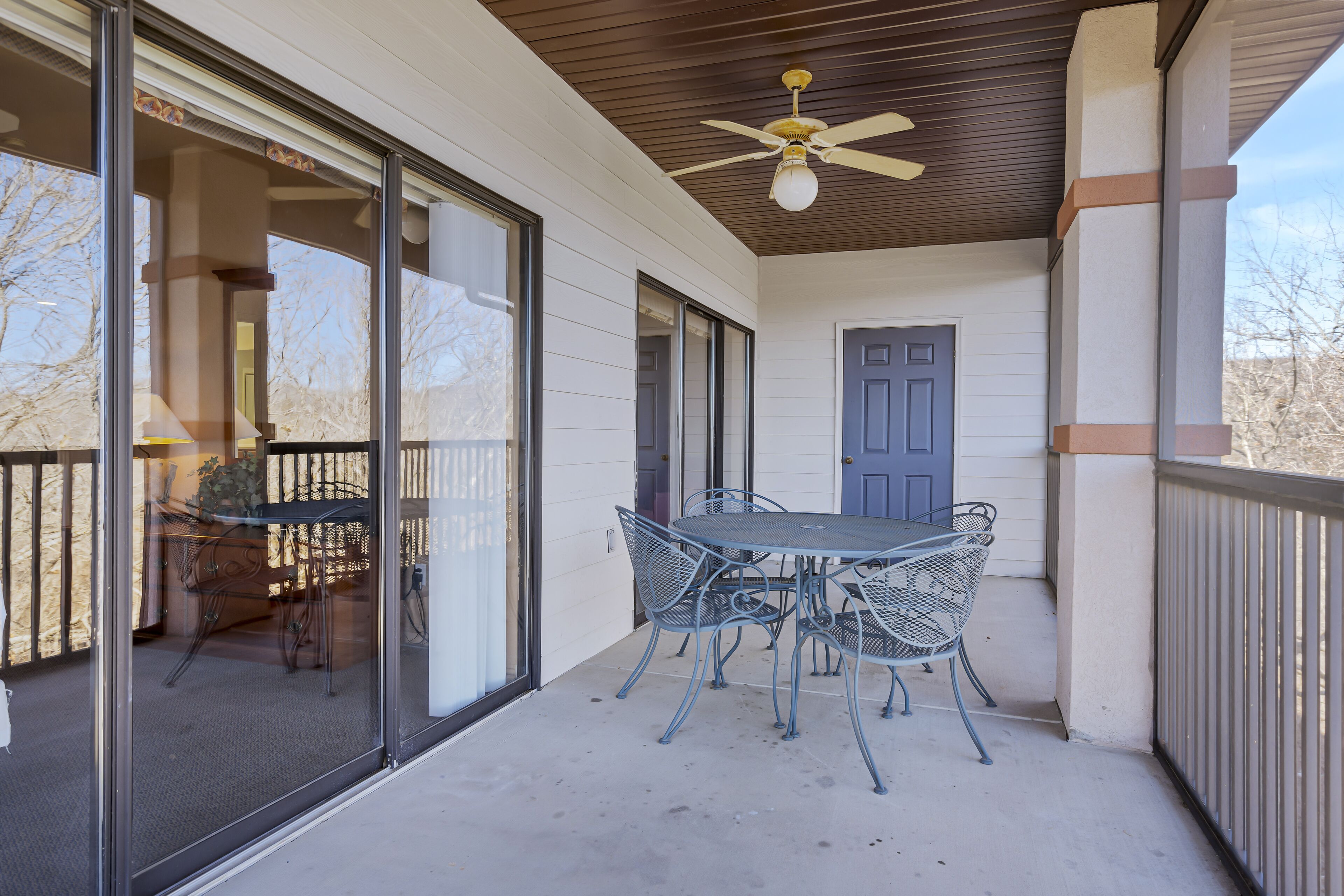 A covered patio with a table and chairs, a ceiling fan, and a door.