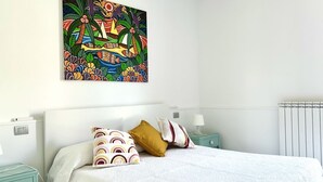 A bedroom with a bed, pillows, a nightstand, a lamp, and a colorful abstract painting on the wall. - M375 - Marcelli, two-room apartment with garden in a residence with swimming poo (Numana)