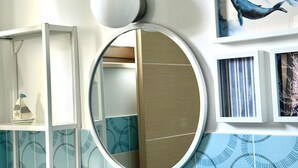 A bathroom with a round mirror, a shelf with decorative items, and a wall with a blue pattern. - M375 - Marcelli, two-room apartment with garden in a residence with swimming poo (Numana)